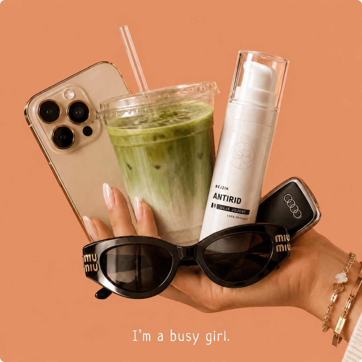 Ruka drži sunčane naočare, ledeni matcha napitak, telefon i Bejzik Antirid, uz natpis „I’m a busy girl.”